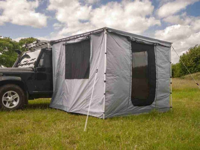 A side awning with an awning room attached underneath on a Land Rover in a grassy UK field.
